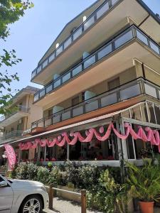 里米尼Hotel Brezza的大楼前有粉红色遮阳篷的餐厅