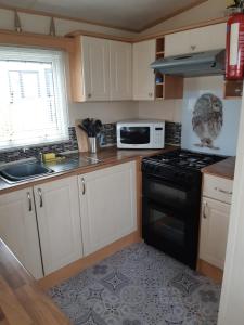 Gilcrux24 The Beeches Caravan Park的厨房配有白色橱柜和黑炉灶烤箱。