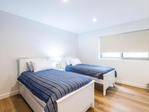 尼尔森湾5 Kingfisher, 5-7 Ondine Close, Nelson Bay, luxury apartment with Wifi and air conditioning的卧室设有两张床,拥有白色的墙壁和木地板