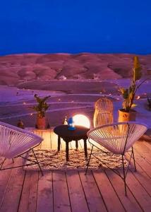 马拉喀什Agafay Luxury camp的海滩上的2把椅子和1张桌子