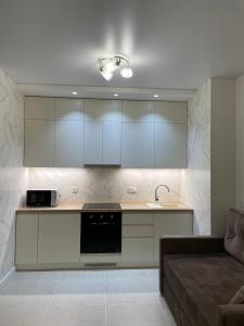 布恰Апартаменти в ЖК Гранд Бурже подобово的厨房配有白色橱柜、水槽和沙发。