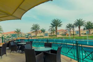 欧奈宰Swiss International Resort Unaizah Al Qassim的游泳池旁带桌椅的天井