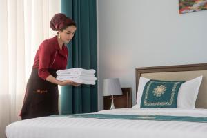 杜尚别Hotel Shumon的把一大堆毛巾放在床边的妇女