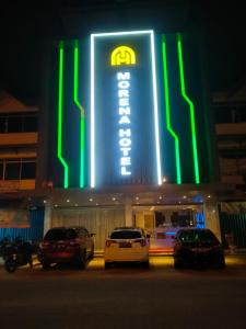 巴淡岛中心Hotel Morena Batam的一座有照明的建筑,前面有汽车停放