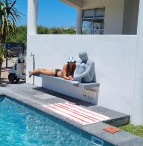 普利登堡湾日光浴普雷特酒店的坐在游泳池旁雕像旁边的床上的女人