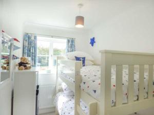 圣梅尔林7 Harlyn Cottages的白色卧室配有白色的婴儿床和泰迪熊