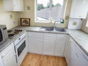 HorrabridgeMoorside的厨房配有白色橱柜、水槽和窗户。