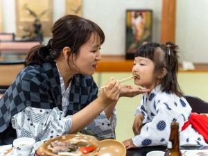 嬉野市初音荘新館的一位用筷子喂小女孩食物的女人
