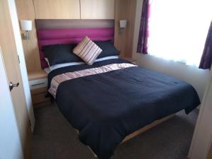 拉尔E3 is a 2 Bedroom 6 berth Lodge on Whitehouse Leisure Park in Towyn near Rhyl close to beach with decking and private parking space This is a pet free caravan的一间卧室配有一张带粉红色床头板的大床