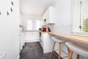 格拉斯哥JOIVY Bright 3-bed flat overlooking The Clyde的厨房配有白色橱柜和带凳子的台面