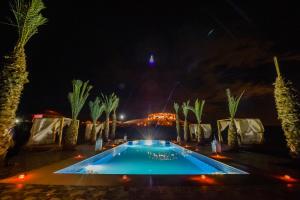 马拉喀什Agafay Pearl Camp Marrakech的棕榈树的夜间游泳池