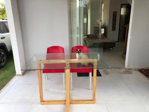因巴塞Casa duplex de temporada em Imbassai的一只猫坐在玻璃桌旁,有两把红色椅子