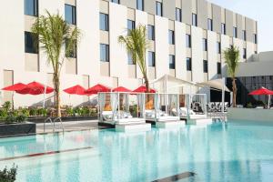 马斯喀特Maani Muscat Hotel & Suites的酒店游泳池拥有棕榈树和红伞