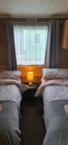 康福斯Carmels Caravan Borwick Lakes的配有窗户和灯的客房内的两张床