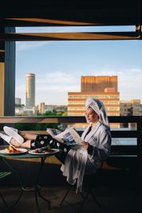 约翰内斯堡Hallmark Hotel by BON Hotels的坐在阳台上读报纸的女人