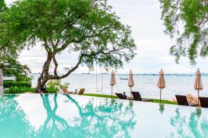 是拉差Centara Sonrisa Residences & Suites Sriracha的水边带遮阳伞和椅子的游泳池