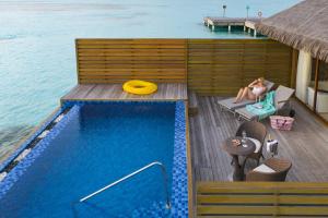 拉薇亚妮环礁Cocoon Maldives - All Inclusive的坐在游泳池旁甲板上的女人