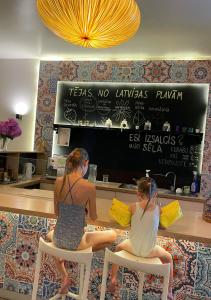 叶卡布皮尔斯柑橘温泉酒店的两个女人坐在柜台前的椅子上