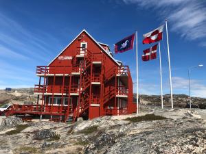 伊卢利萨特HOTEL SØMA Ilulissat的一块红色的建筑,在一些岩石上,有旗帜