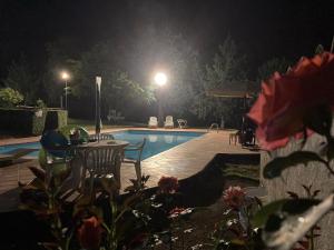 SassoMasseria Le Zavattole的游泳池在晚上配有桌椅