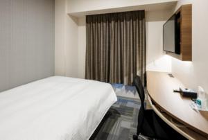 冈山Smile Hotel Okayama的酒店客房配有一张床和一张书桌及一台电视