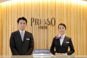 东京Keio Presso Inn Shinjuku的两人穿着西装站在墙上