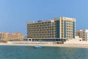 拉斯阿尔卡麦Radisson Resort Ras Al Khaimah Marjan Island的一艘蓝色的船在大建筑前的水中