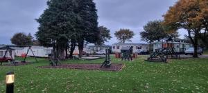Gilcrux24 The Beeches Caravan Park的一个带秋千的公园和一个草地上的游乐场