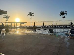 阿拉亚尔-杜卡布Golden Lake Apart Hotel Arraial do Cabo的棕榈树泳池和日落背景
