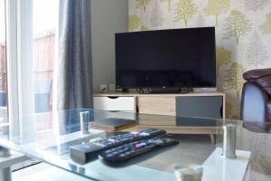 诺里奇Queens Lodge - Beautiful Modern House with Free Parking - Marvello Properties的一张玻璃桌、电视和两个遥控器
