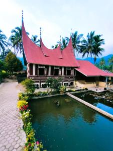 BasoRumah Gadang Simarasok的池塘旁有红色屋顶的房子