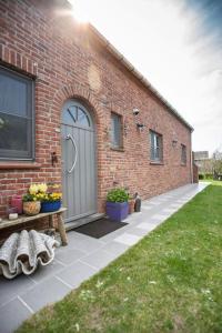 德哈恩Zalig Cosy appartement 2-4 pers.fietsen & tuin的砖砌的建筑,有灰色的门和长凳