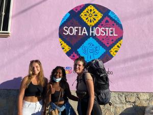 卡波圣卢卡斯Sofia Hostel Cabo的站在粉红色墙前的三个女人