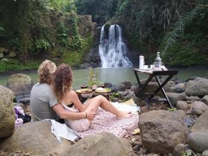 塔巴南Galalima Glamping的两个女人坐在瀑布前的岩石上