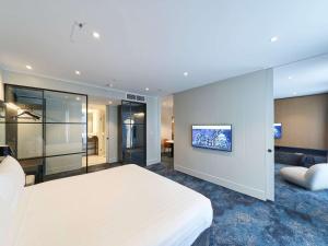 阿德莱德阿德莱德铂尔曼酒店的卧室配有白色的床和墙上的电视