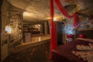 Guzelyurt卡帕多西亚古董吉维利洞穴酒店的洞穴内的一个房间,配有床和红色窗帘