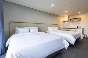 济州市Aewol Stay in Jeju Hotel&Resort的配有白色床单的酒店客房内的两张床