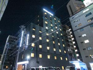 名古屋HOTEL LiVEMAX Nagoya Kanayama的一座高大的建筑,晚上在城市里装有窗户