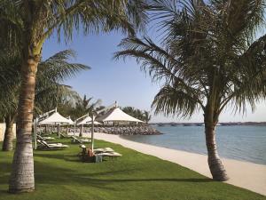 阿布扎比Shangri-La Hotel Apartments Qaryat Al Beri的棕榈树、椅子和遮阳伞的海滩