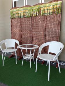 克提Homestay Qaseh Kerteh的三把白色椅子和一张桌子,墙上铺有绿色地毯