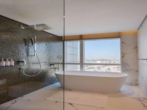 迪拜Movenpick Jumeirah Village Triangle的一间带浴缸和淋浴的浴室,并设有一个窗户