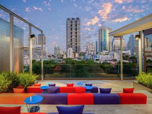 曼谷ibis Styles Bangkok Silom的一个带红色和蓝色家具的屋顶露台,享有城市天际线