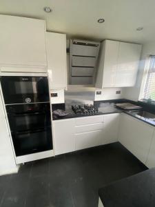 卢顿Theldon的厨房配有白色橱柜和黑炉灶烤箱。