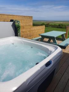 奥克尼Lilly's Lodges Orkney Robin Lodge的甲板上的热水浴缸和野餐桌