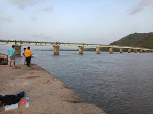 阿利鲍格Parvati Niwas Homestay -Nearby Revdanda Beach & Fort - WiFi available的两个人站在河岸边,有一座桥