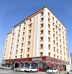 锡卜Jarzez Hotel Apartments Al Hail的一座白色的大建筑,前面有汽车停放