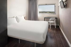 阿尔巴塞特B&B HOTEL Albacete的卧室配有白色的床、桌子和窗户。