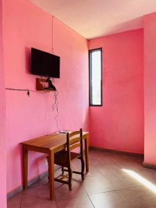 AntsakomboenaLE JAVA的一间设有木桌和粉红色墙壁的客房