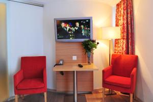 采尔马特阿里斯特拉瑞士弗莱尔酒店的一间设有两张红色椅子和一张桌子及电视的房间