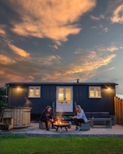 彭里斯Inglewood Shepherd's Huts的两个人坐在一个小房子前面的火坑旁